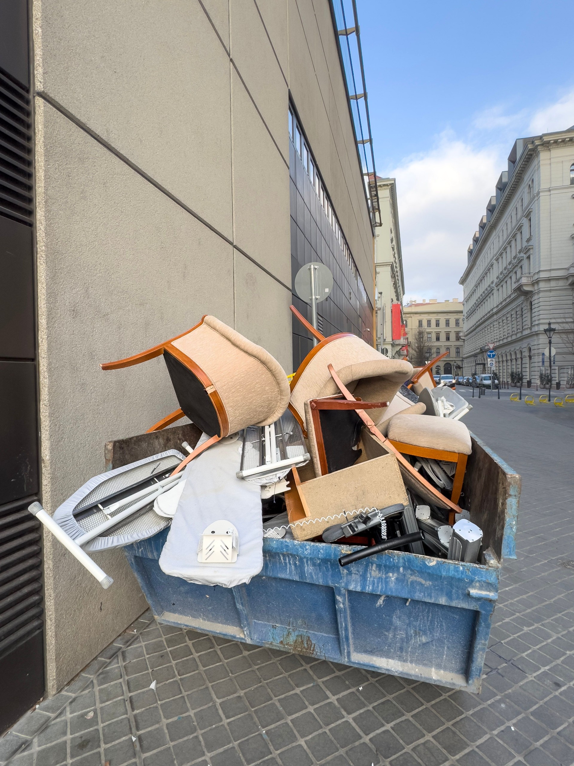 Discarded Furniture and Household Items in a Dumpster on Urban Sidewalk, Symbol of Urban Waste and Renewal